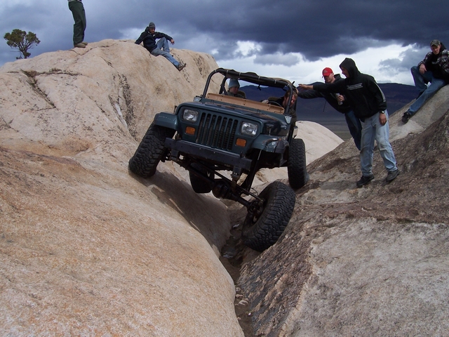 Dark green Jeep Wrangler climbing a rocky incline with people watching