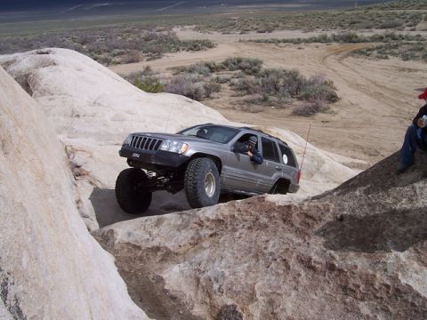 1989 Ford Bronco - Jeep Grand Cherokee tackling a difficult off-road trail with large boulders.