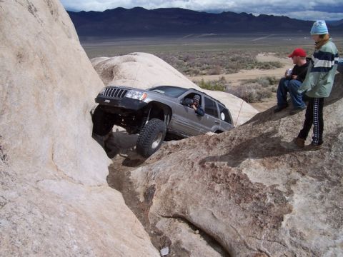 1989 Ford Bronco - A Jeep Grand Cherokee navigates a rocky trail with spectators observing the challenging terrain.