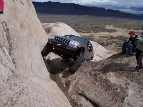 1989 Ford Bronco - A Jeep Grand Cherokee navigates a challenging rocky terrain in a desert landscape.