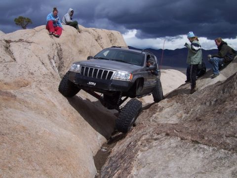 1989 Ford Bronco - Modified Jeep Grand Cherokee tackling a difficult off-road obstacle with spectators watching.