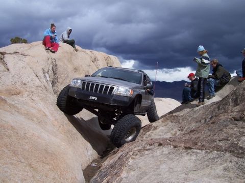1989 Ford Bronco - A Jeep Grand Cherokee navigates a rocky trail with spectators observing the action.