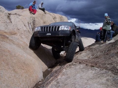 1989 Ford Bronco - A Jeep Grand Cherokee navigates a rocky terrain with people watching from above.