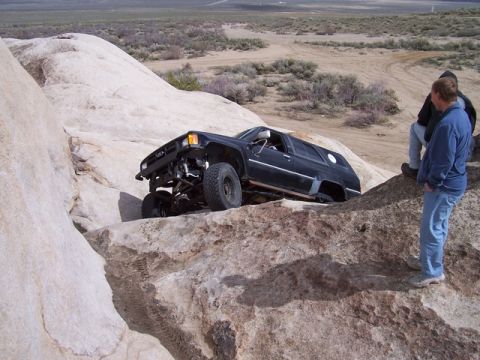 1989 Ford Bronco - Modified black SUV tackling a challenging rock crawling course in a desert landscape.