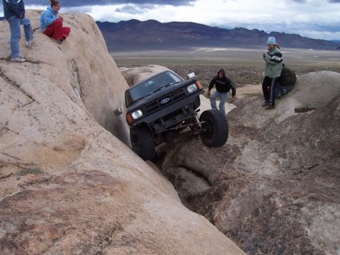 1989 Ford Bronco - A modified Ford Bronco navigates a rocky trail with onlookers observing the challenging off-road maneuver.