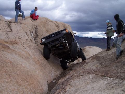 1989 Ford Bronco - A black Ford Bronco navigates a steep, rocky terrain with onlookers observing the challenging climb.