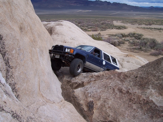 Blue SUV with white top is crawling over large rocks in a desert landscape