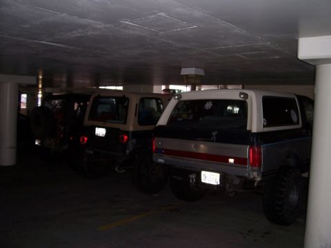 1989 Ford Bronco - Multiple SUVs are parked in a dimly lit garage, with one Ford Bronco prominently visible from the rear.