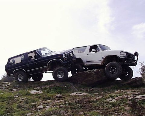 1985 Ford Bronco - Two Ford Broncos navigate a rocky incline under a cloudy sky.