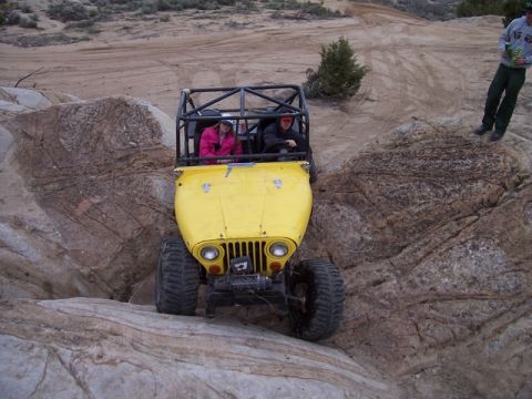 1989 Ford Bronco - A yellow off-road vehicle with a roll cage is driven over rocks during an outing.