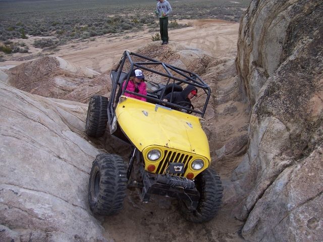 Yellow off-road buggy with roll cage navigating a rocky trail, two people inside