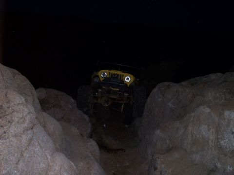 1989 Ford Bronco - A yellow Jeep Wrangler navigates a rocky path in the dark.