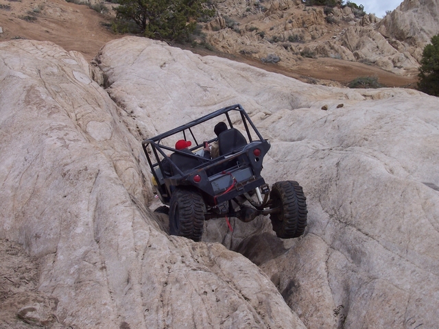 Buggy with roll cage climbing up a rocky incline. Two people are inside