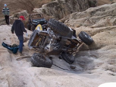 1989 Ford Bronco - An off-road vehicle is stuck on a rocky incline, with another Jeep and onlookers present.