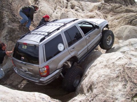 1989 Ford Bronco - A Jeep Grand Cherokee tackles a challenging rocky trail with assistance from onlookers.
