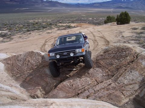 1989 Ford Bronco - A dark blue Ford Bronco navigates a rocky off-road course in a desert landscape.