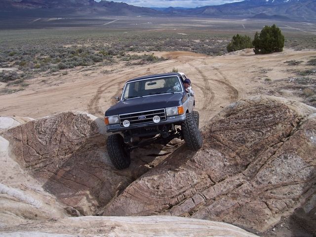 Dark blue lifted Ford Bronco descending a slickrock ledge on a desert trail