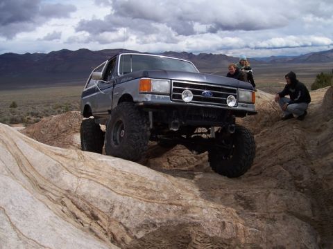 1989 Ford Bronco - A heavily modified 1987 Ford Bronco tackles a challenging off-road course with onlookers present.