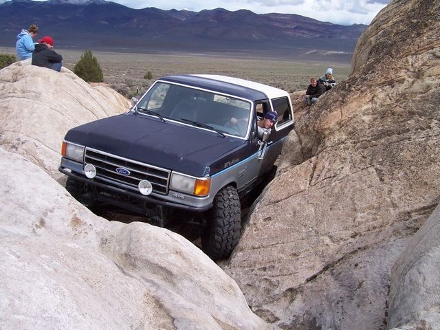 Dark blue Ford Bronco with white top navigating a rocky trail. Driver is looking out the window
