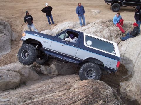 1989 Ford Bronco - A 1989 Ford Bronco navigates a rocky off-road course, with onlookers observing the challenging terrain.
