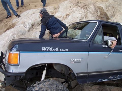 1989 Ford Bronco - A two-tone Ford Bronco is stuck on a rocky incline, with a person exiting through the driver's side window.