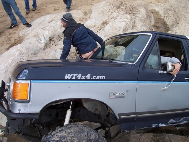 1989 Ford Bronco stuck on rocks with a person climbing out the window