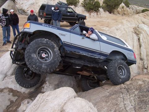1989 Ford Bronco - This heavily modified SUV is navigating a rocky trail, with a group of onlookers and another vehicle in the background.