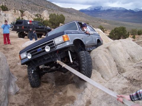 1989 Ford Bronco - A gray Ford Bronco navigates a rocky off-road course with a black SUV in the background.