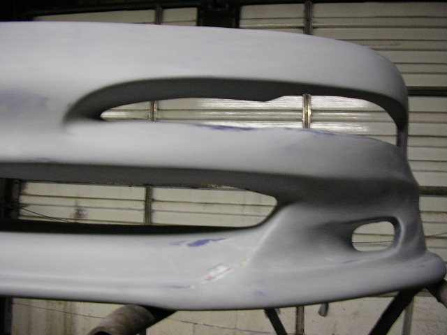 primer-coated car bumper with two large openings and a smaller fog light opening