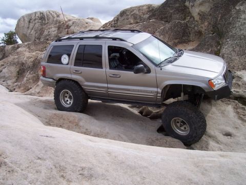 1989 Ford Bronco - Jeep Grand Cherokee navigates rocky terrain with lifted suspension and oversized tires.