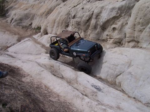 1989 Ford Bronco - Jeep Wrangler tackling a challenging off-road course with large rocks and steep inclines.