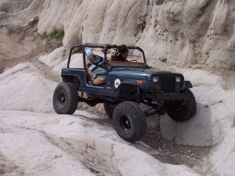 1989 Ford Bronco - A Jeep Wrangler tackles a challenging rocky terrain, with two occupants inside the vehicle.
