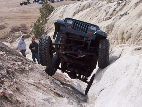1989 Ford Bronco - A Jeep Wrangler navigates a rocky trail, its off-road capabilities. Other vehicles and people are visible in the background.