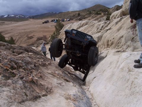 1989 Ford Bronco - A black Jeep Wrangler is precariously balanced on a rock formation during an off-road excursion.