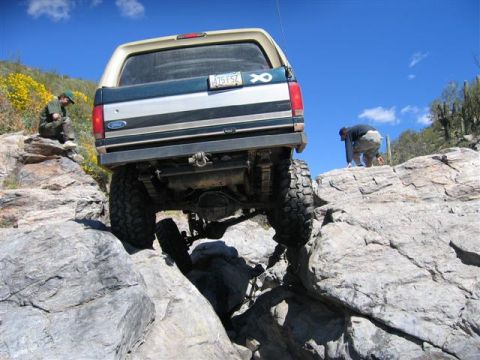 1994 Ford Bronco - A modified Ford Bronco tackles a challenging rocky trail under a bright blue sky.