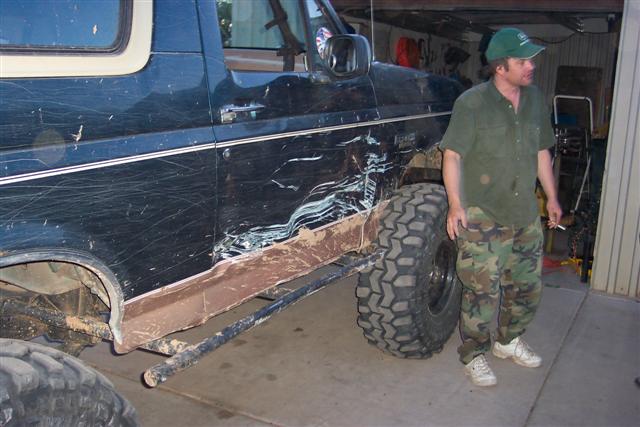 Dark blue lifted Bronco with crushed rocker panel and bent rock slider in a garage