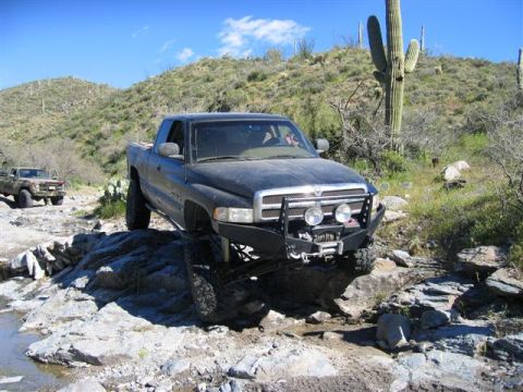 1994 Ford Bronco - A black Dodge Ram pickup truck is shown navigating a rocky trail in a desert landscape with saguaro cacti.