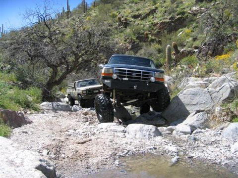 1994 Ford Bronco - Two trucks, a 1994 Ford Bronco and an older pickup, tackle a challenging off-road path.