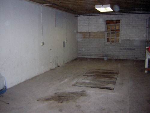Interior of a room with concrete floor, white walls, and a boarded-up window