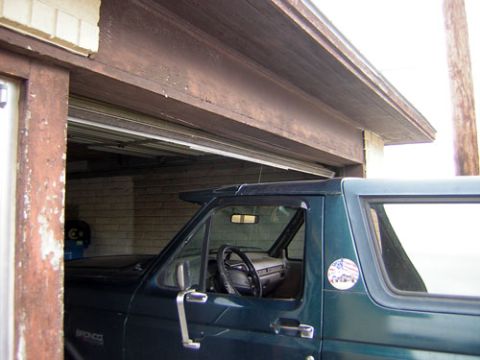 1995 Ford Bronco - Driver-side view of a dark green full-size Ford Bronco nosed into a garage, with its removable hardtop, rear quarter window and a 'Bronco'…