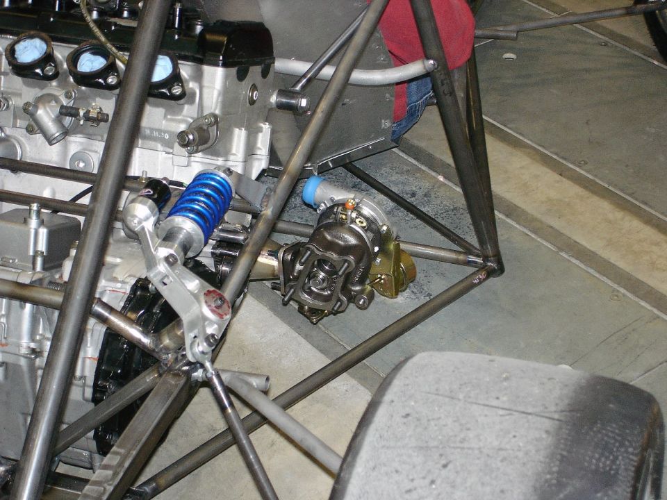 Racing car chassis with engine, blue coilover shock, turbocharger, and slick tire