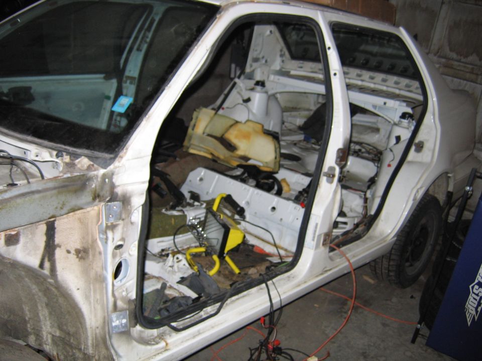 Interior of a dismantled white car, showing exposed frame and wiring