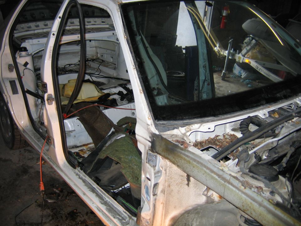 Interior of a dismantled car, showing stripped door panels, exposed wiring, and rusted components