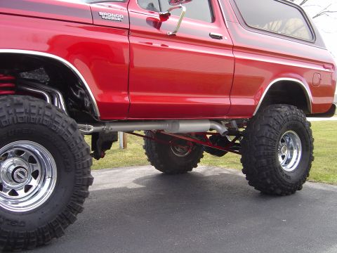 1978 Ford Bronco - Low side view of a lifted red Ford Bronco with a BRONCO RANGER fender badge and hardtop, showing the exposed undercarriage: a side-exit exh…