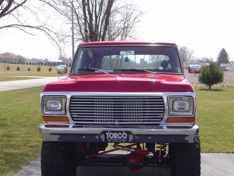 1978 Ford Bronco - This red pickup truck features a prominent grille and lifted suspension, with another vehicle visible in the distance.