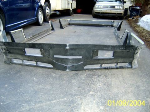 1973 Ford Ranchero - An aftermarket car bumper is laid out on a driveway, with other vehicles visible in the background.