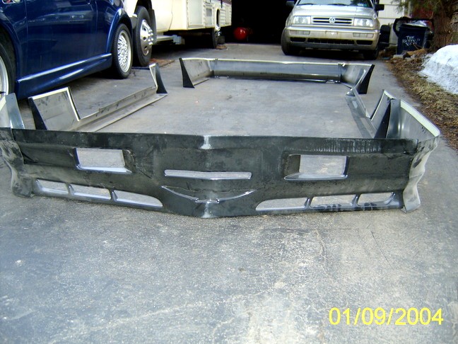 Black aftermarket car bumper with rectangular cutouts and horizontal vents