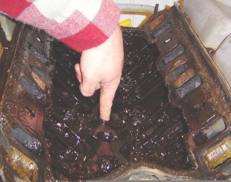 Finger pointing at thick black oil sludge coating engine internals