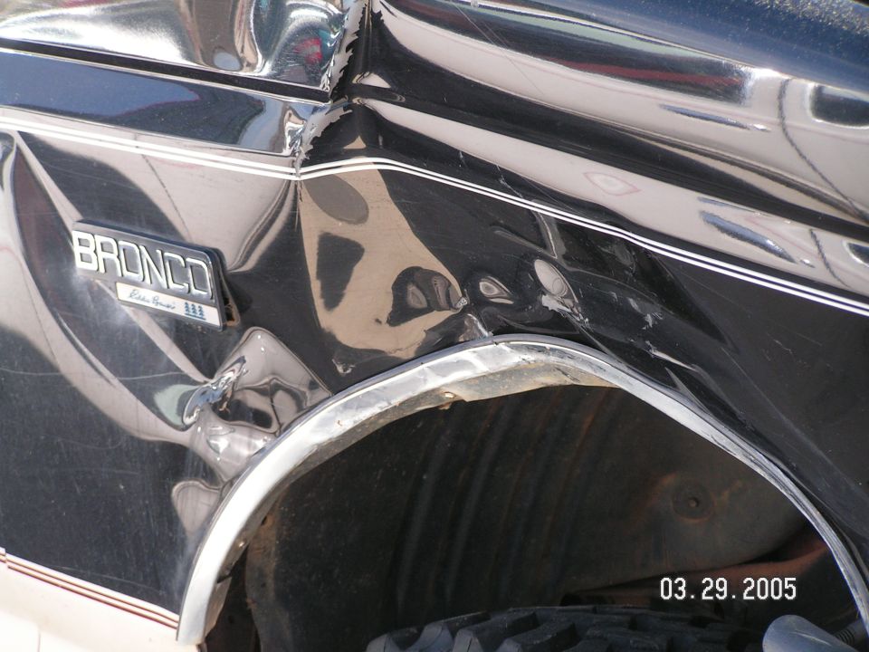 Damaged rear quarter panel of black Bronco with creased, dented sheet metal above wheel arch