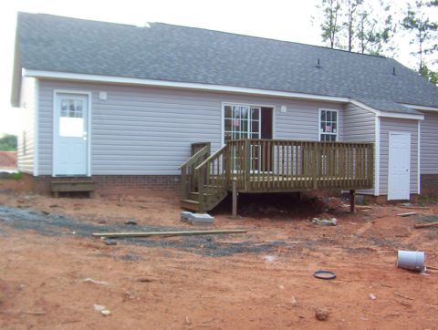 1986 Ford Bronco - A house under construction features a wooden deck and siding, with a dirt yard surrounding it.